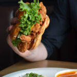 A hand holds a chicken burger at Fergus and Bix